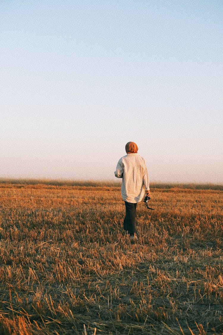 A Woman Walking On A Meadow At Sunset 