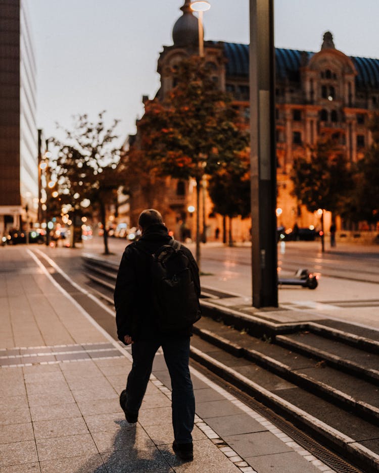 Back View Of A Man Walking On The Sidewalk In City In The Evening 