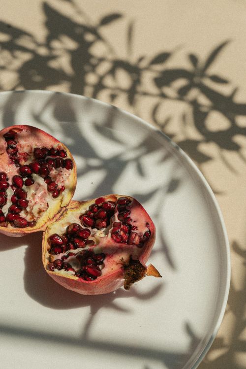 Free Artistic arrangement of pomegranate halves casting shadows on a plate under natural light. Stock Photo