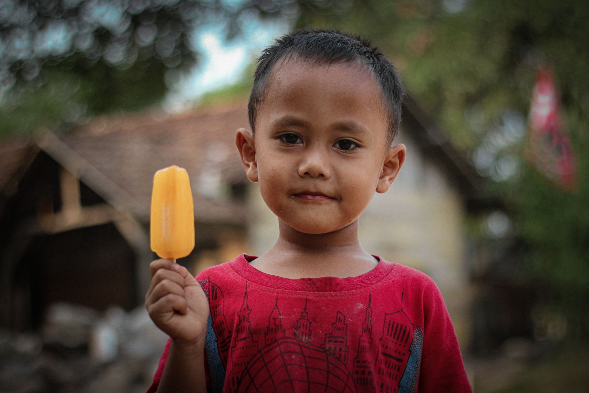 Young boy in a red shirt enjoying a yellow ice cream in a rural village in Indonesia.