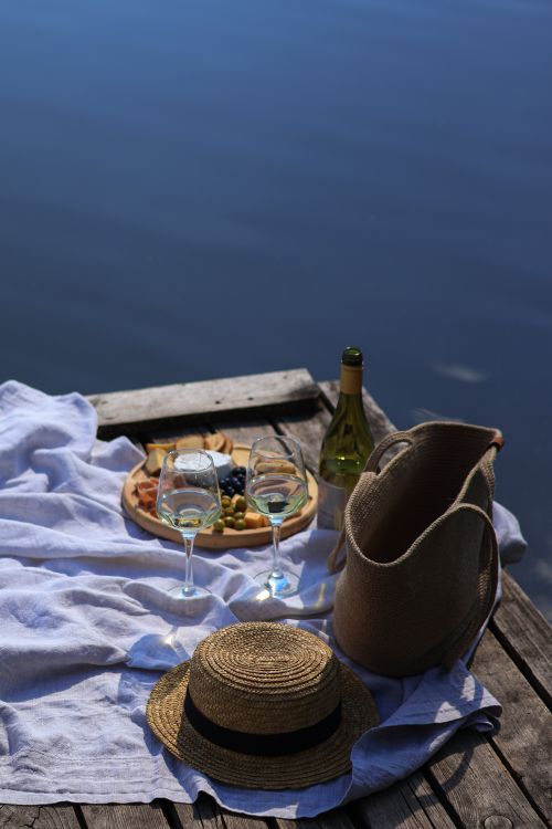Free Charming lakeside picnic scene with wine, fruit, and cheese under the sun, ideal for relaxation. Stock Photo