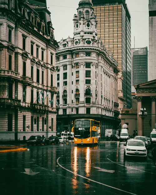 Free A vibrant urban scene featuring historic architecture amidst rain, with vehicles reflecting on wet streets. Stock Photo