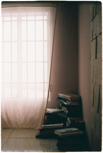A stack of books by a softly lit window in a quiet, serene room.