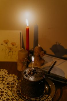 Warm candlelit setup with a chocolate cake, sculpture, and vintage decor in soft focus.