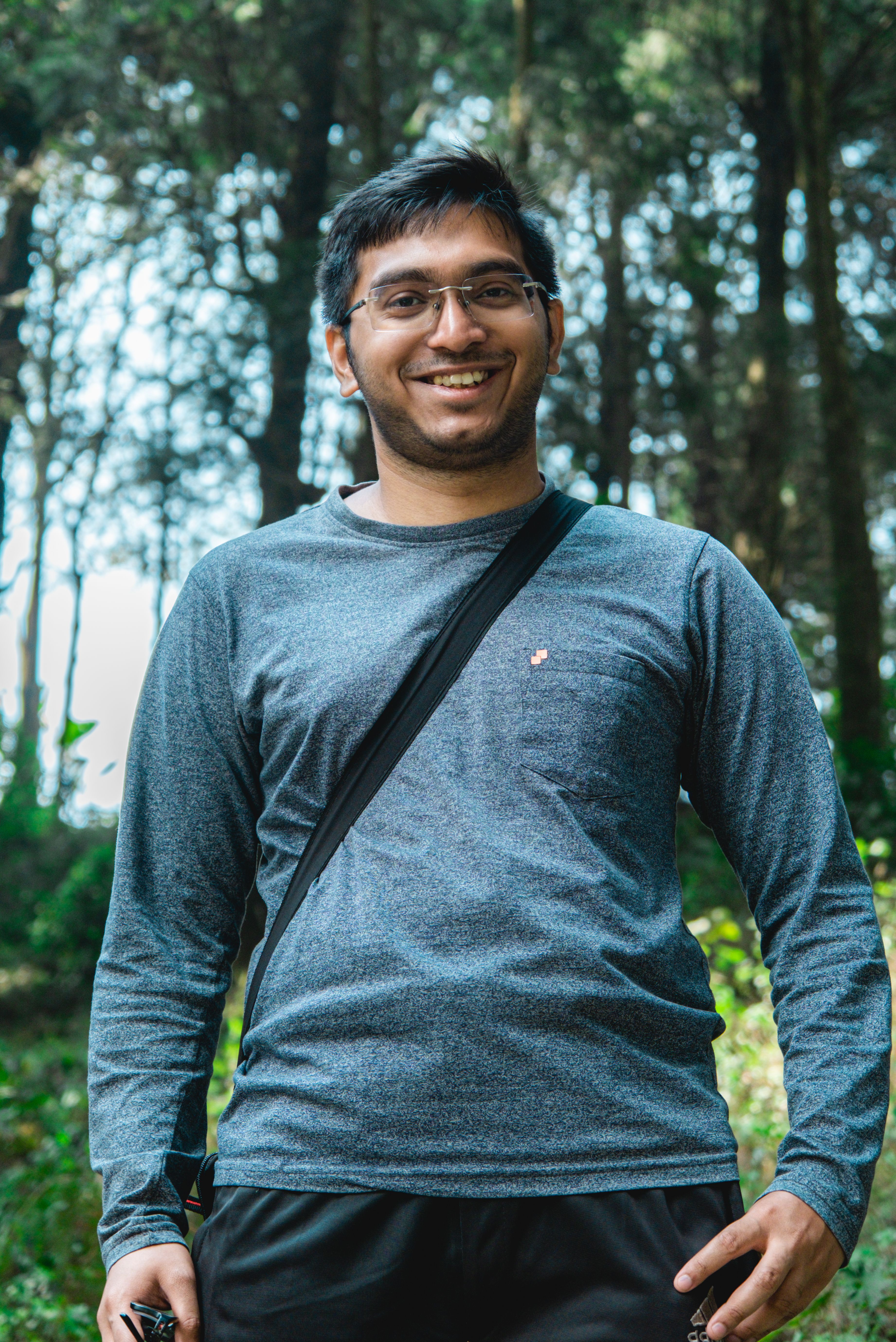 Portrait of a smiling man with eyeglasses standing in the forest holding a camera.