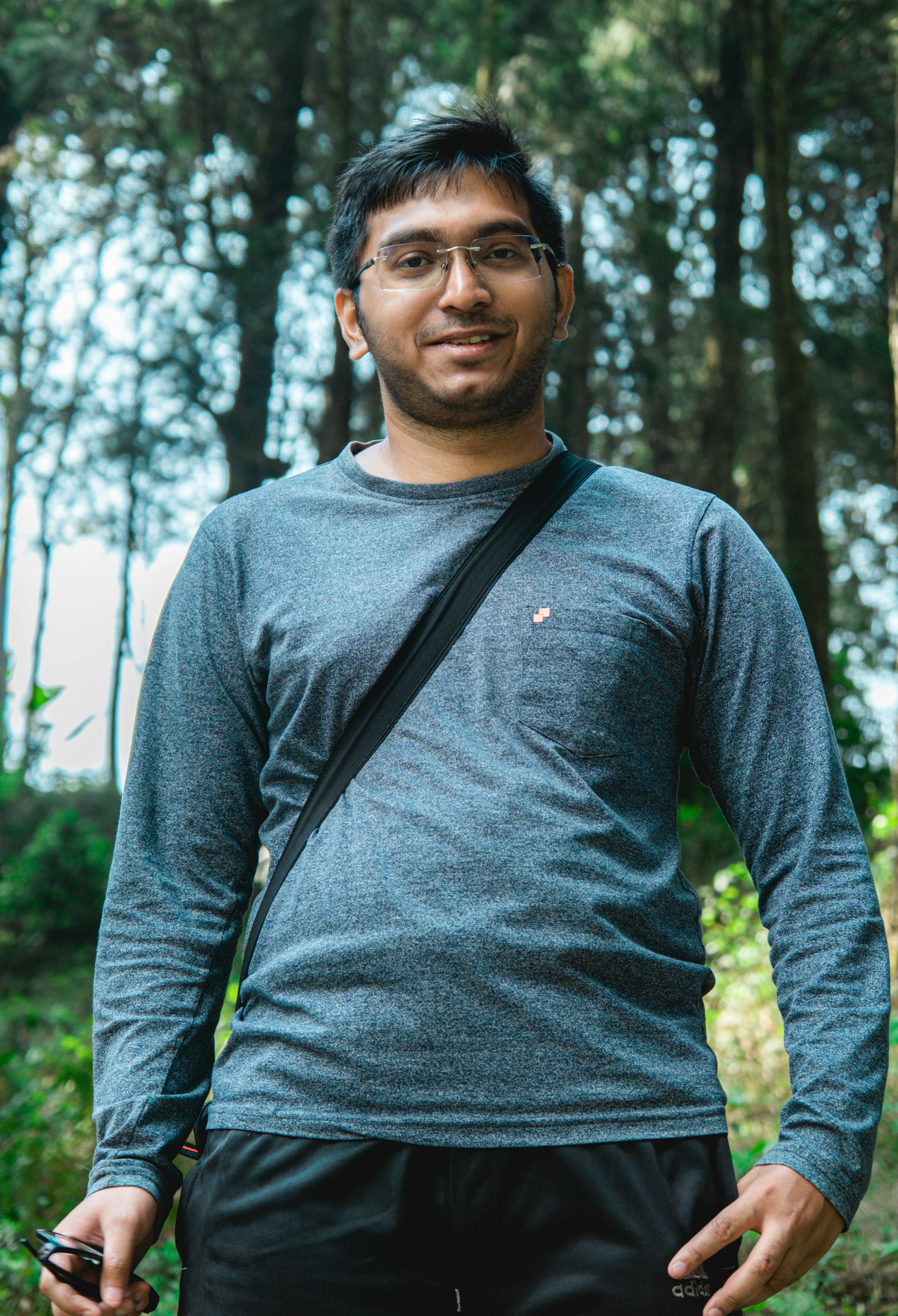 Portrait of a young man smiling, standing confidently in a lush forest backdrop.