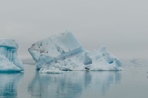 Free A tranquil view of icebergs floating in calm, reflective Arctic waters. Stock Photo