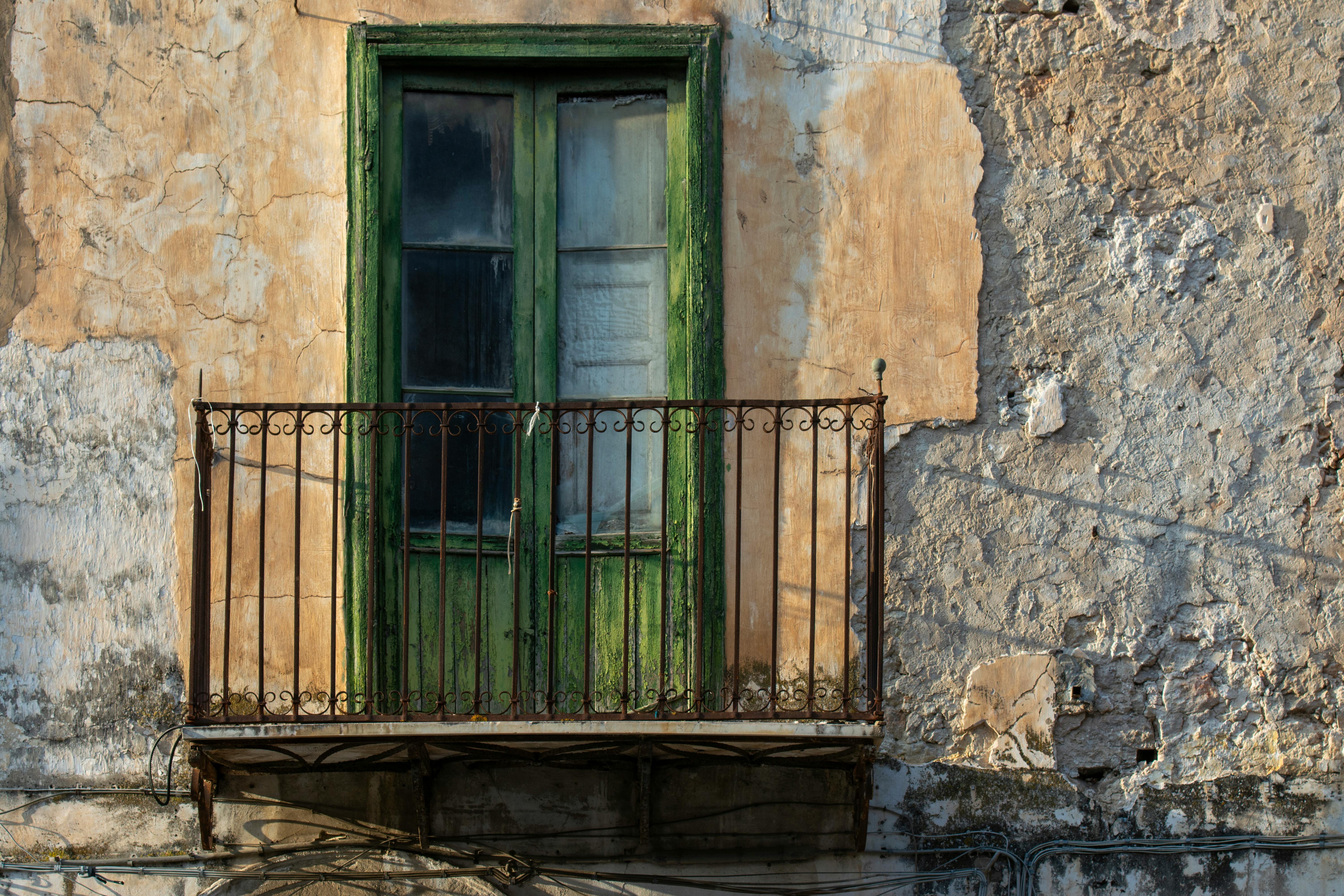 A rustic balcony featuring a weathered green door set against an old, textured wall.