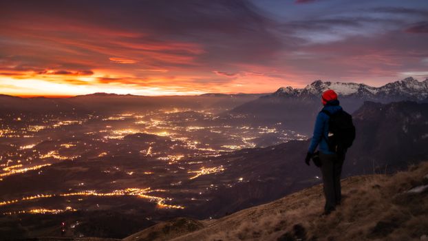 A hiker enjoys a breathtaking sunset view over a sparkling mountain cityscape.