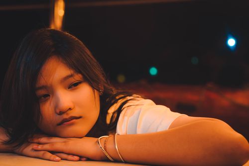 Free A teenage girl lying on a table, illuminated by warm light, gazing thoughtfully. Stock Photo