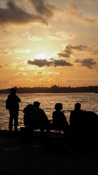 Silhouetted figures watch a stunning sunset over the sea, creating a calm and picturesque scene.