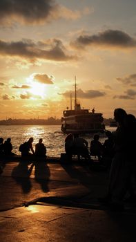 Silhouetted figures enjoying a sunset by the harbor in Istanbul, with a ship in the background.