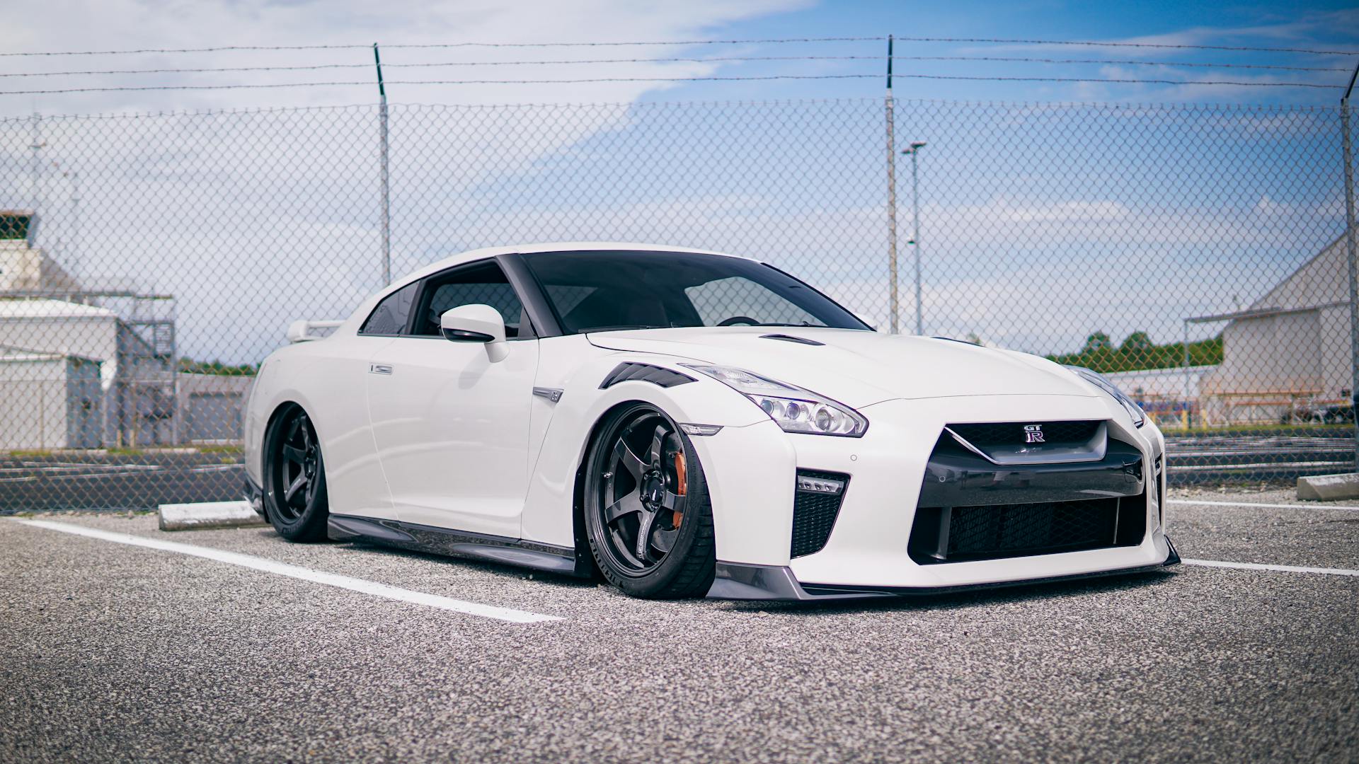 A customized white Nissan GT-R parked in an urban parking lot, emphasizing its sporty design.