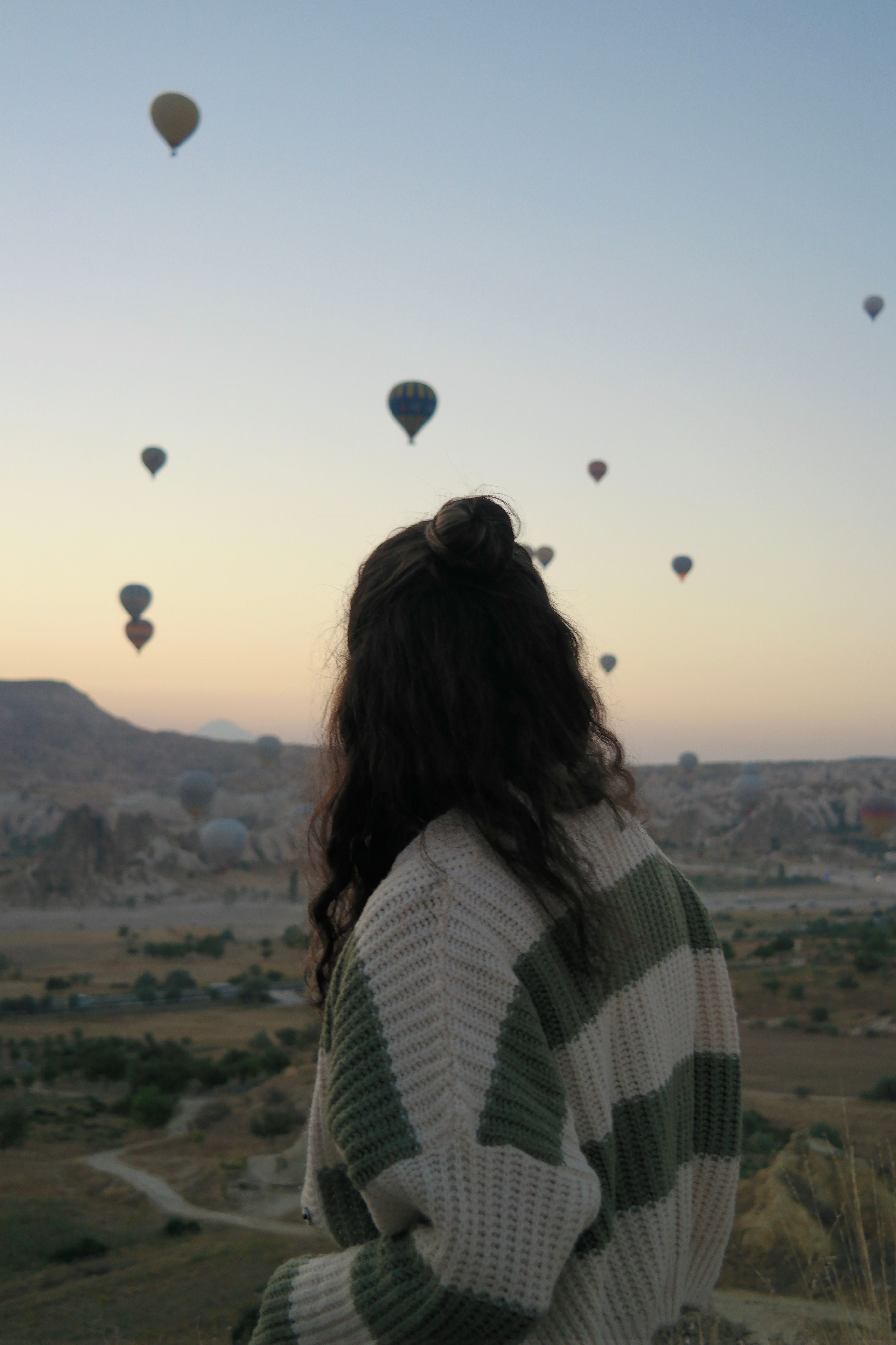 Woman gazing at hot air balloons over Cappadocia's unique landscape at sunset.