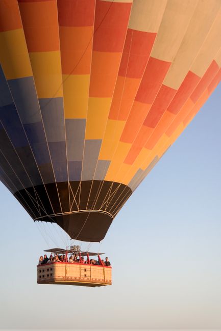 A vibrant hot air balloon with passengers floating in a clear blue sky during the day.