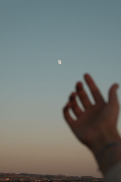 Free Blurred hand reaching up to the sky towards a visible moon during twilight. Stock Photo