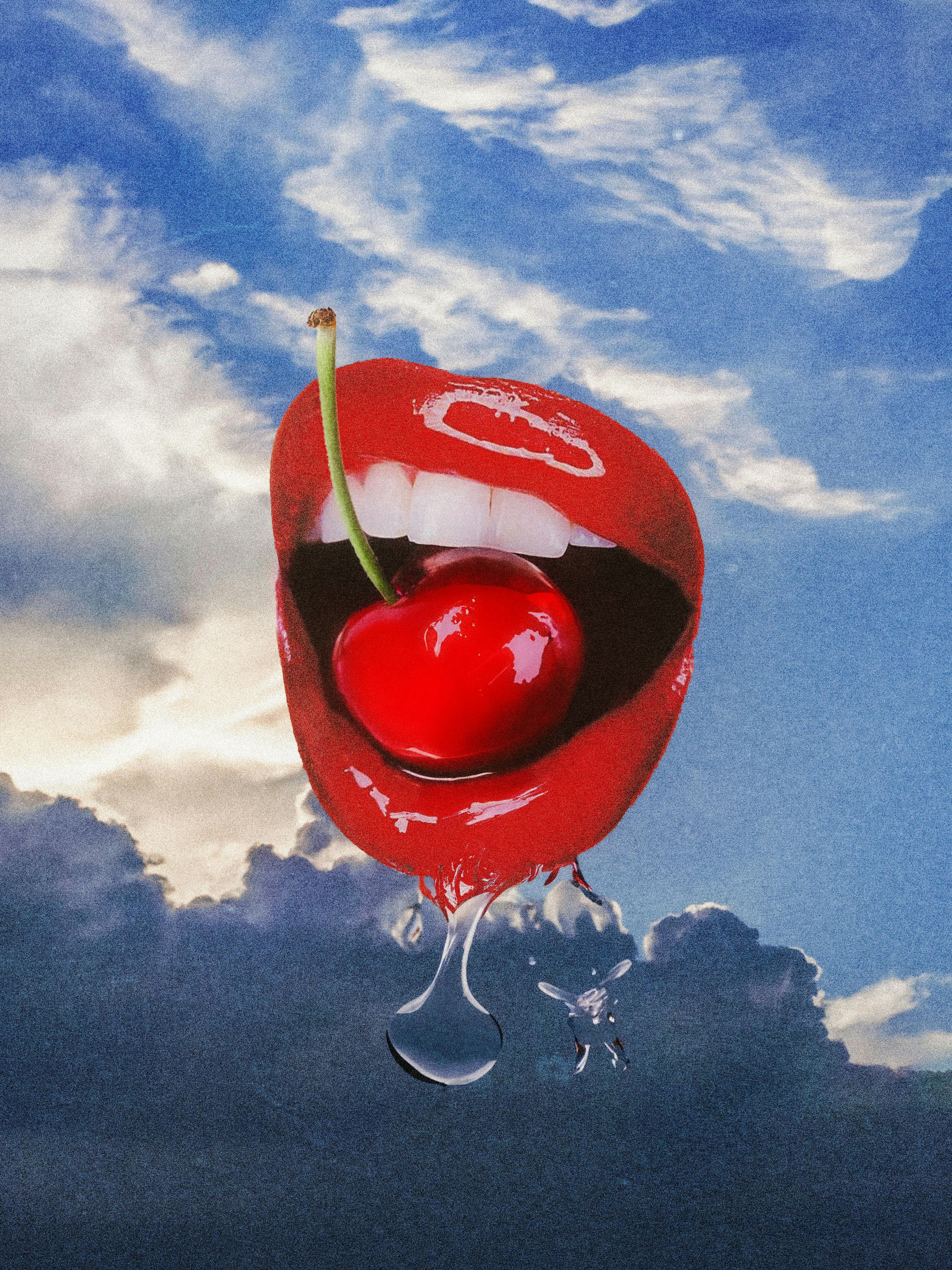 Vibrant red lips holding a cherry set against a dramatic cloudscape, with a creative and surreal vibe.
