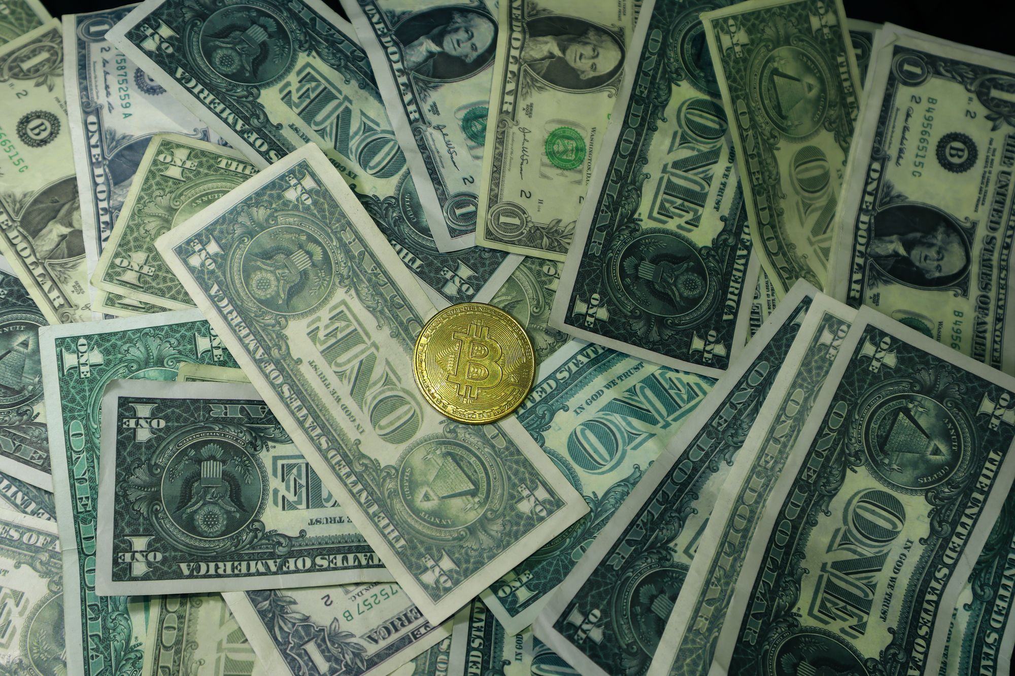 Moneda con el símbolo de bitcoin junto a billetes de dólares estadounidenses