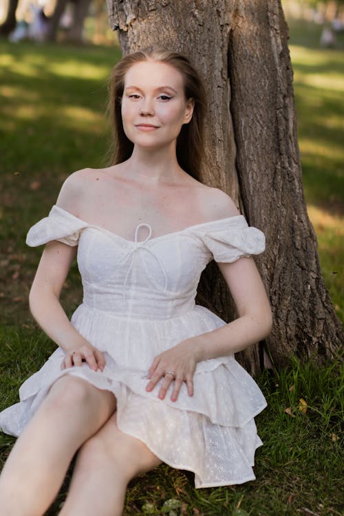 Young Woman in a White Dress Sitting under a Tree in a Park 