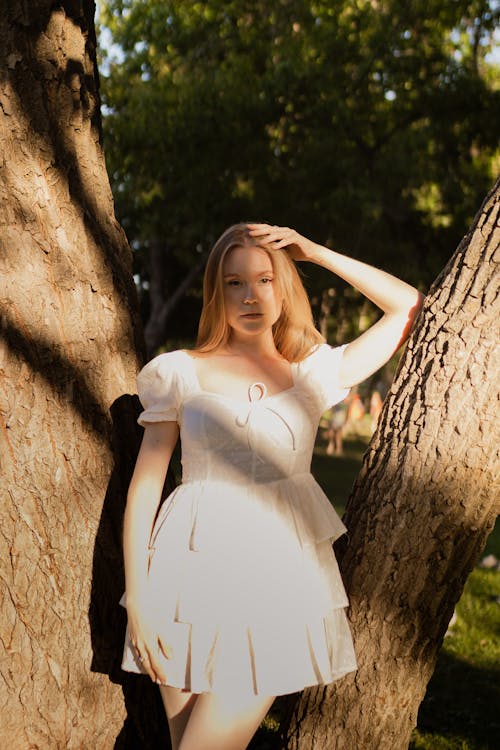 Beautiful Young Woman in White Dress Posing Near Tree