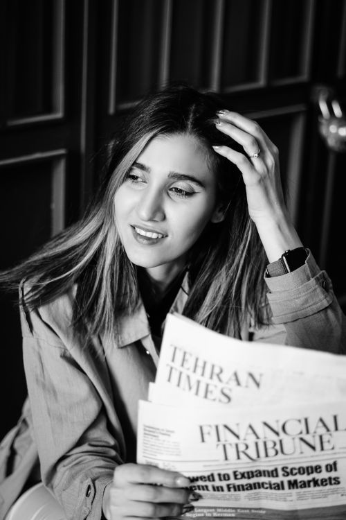Free Black and white portrait of a woman reading Tehran Times newspaper, touching her hair. Stock Photo