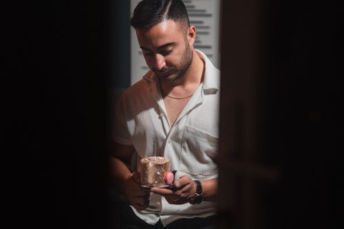 Free A man in a white shirt carefully holds a small elegant cake in a dimly lit room. Stock Photo