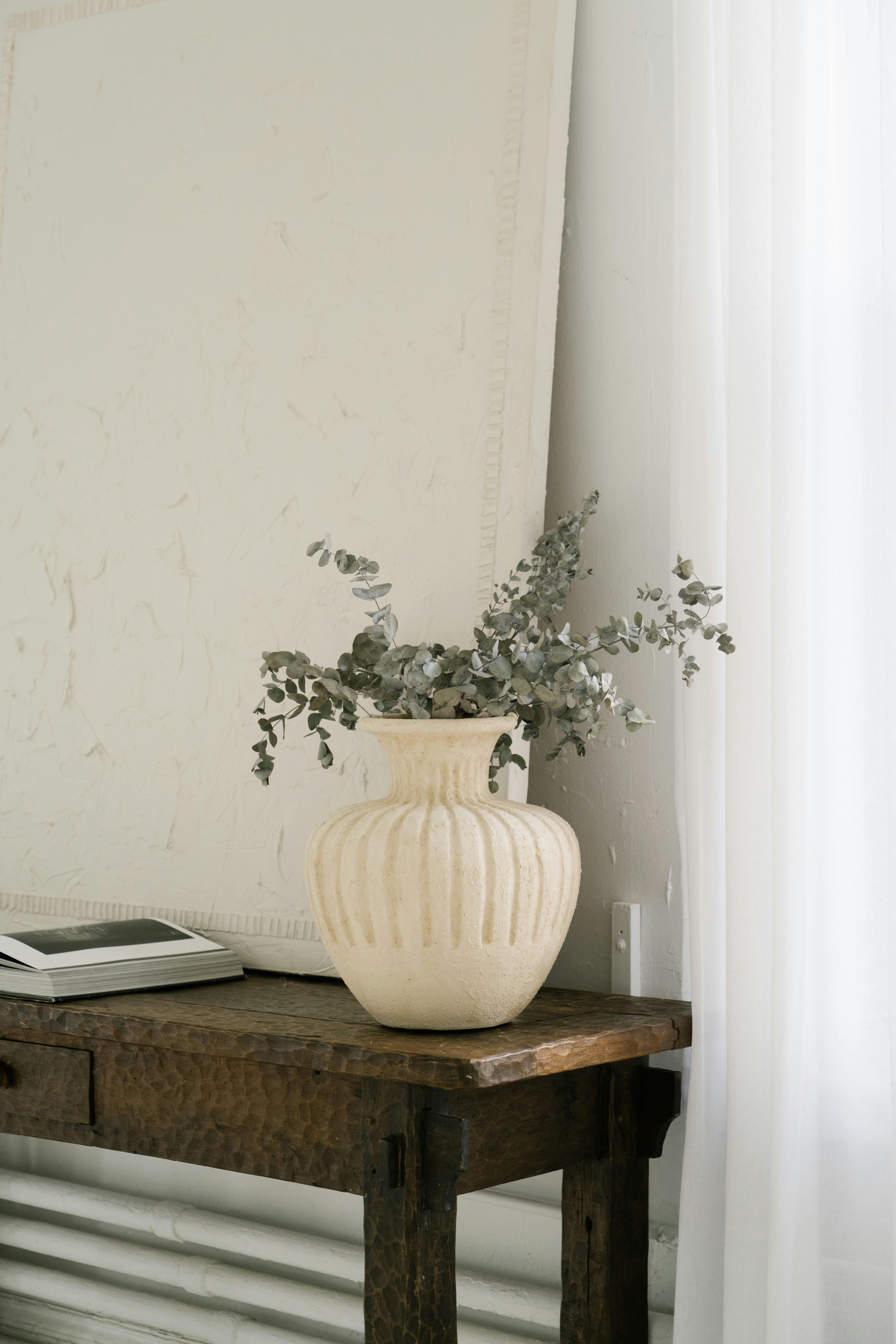 Elegant still life featuring a ceramic vase with eucalyptus on a wooden table in a minimalist room.