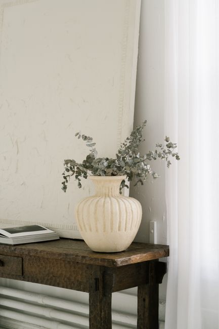 Elegant still life featuring a ceramic vase with eucalyptus on a wooden table in a minimalist room.