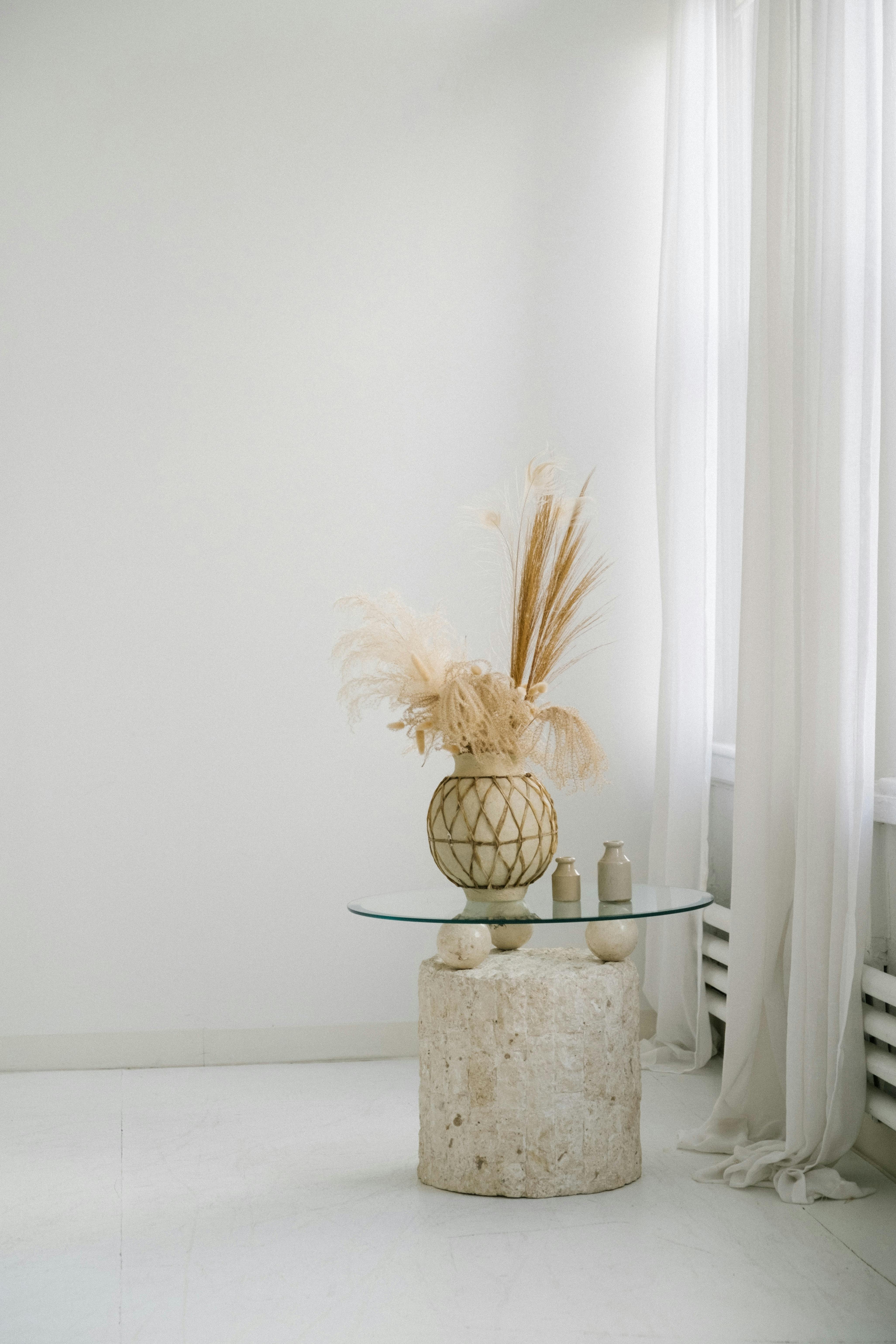 Elegant minimalist interior featuring dried floral arrangement in a vase on a glass-topped table.