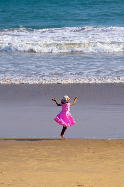 Little Girl in Pink Dress on Beach Looking at Waves