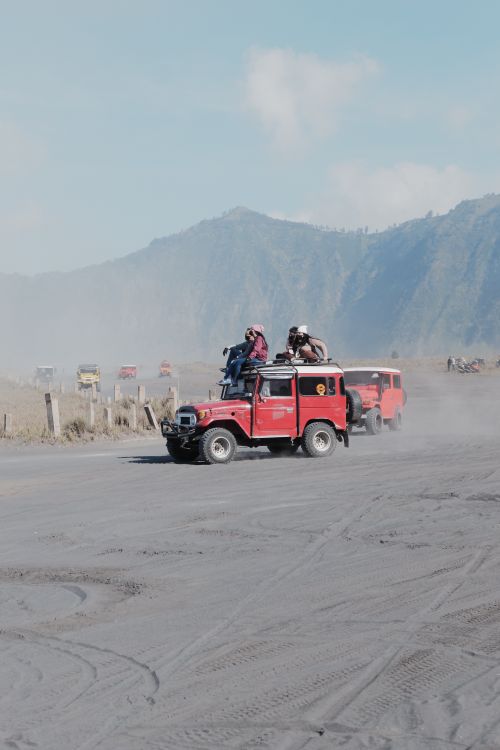 Free Jeeps driving through dusty terrain with a backdrop of Mount Bromo, perfect for adventure travel enthusiasts. Stock Photo