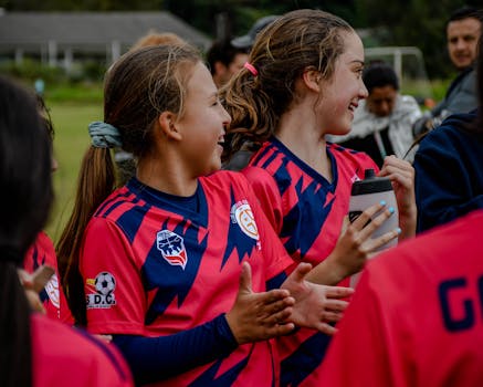 Happy young girls in sportswear celebrating a soccer match victory on an outdoor field.