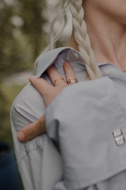 Close-up of a woman's hand on shoulder with a stylish braid and rings in focus.