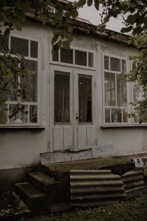 Free A rustic, countryside house entrance with a vintage facade and overgrown steps. Stock Photo