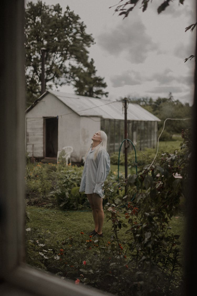 Young Blonde Woman In Light Blue Shirt Standing In A Rural Yard