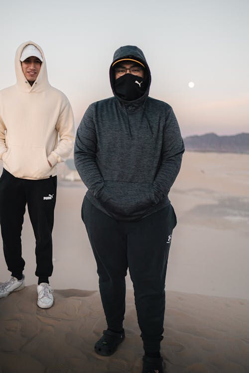 Two people wearing hoodies and masks standing in the desert