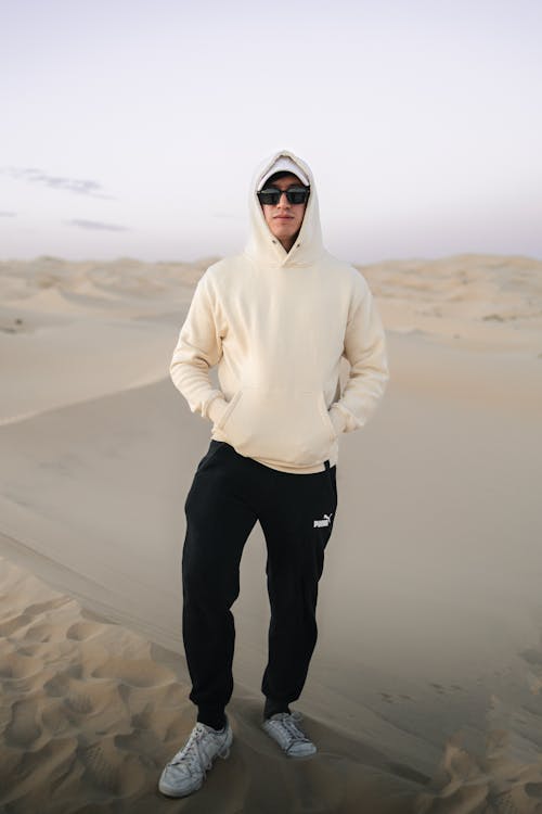 A man in a white hoodie and black pants standing in the desert