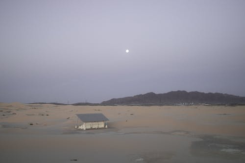 A small house in the desert with the moon in the background