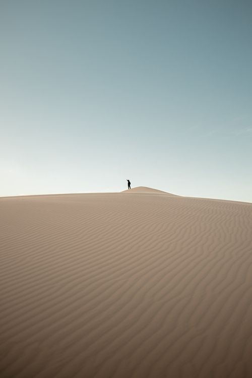 Free A solitary figure atop the Samalayuca dunes under a vast desert sky. Stock Photo
