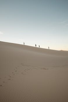 Four people trekking across the vast Samalayuca sand dunes at sunset.