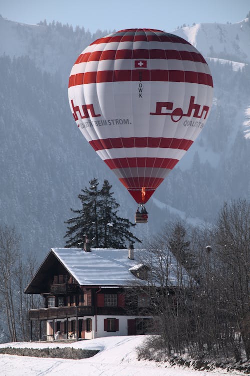A Hot Air Balloon Flying over a House and Valley Covered in Snow 