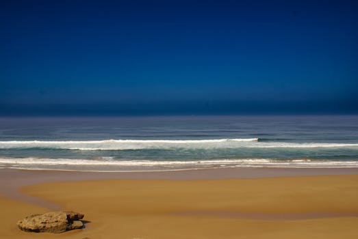 A tranquil beach scene with gentle waves and a vibrant blue sky. Perfect for relaxing atmospheres.