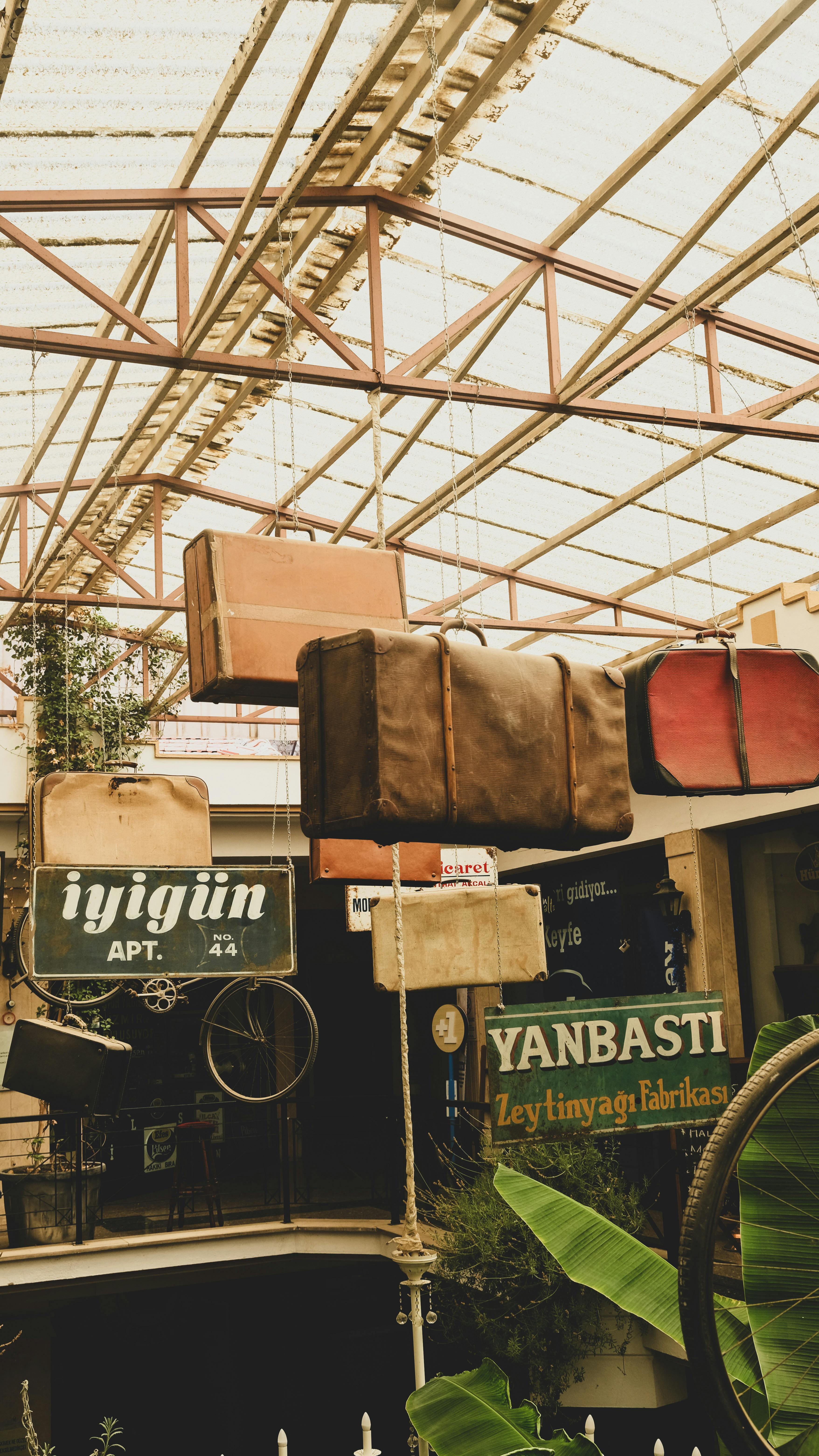 A collection of vintage suitcases hanging from ceiling in a rustic market setting with old signs.