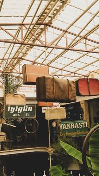 A collection of vintage suitcases hanging from ceiling in a rustic market setting with old signs.