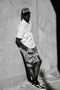 Stylish man in Ankara wearing patterned shorts poses against a wall.