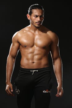 Fit male model posing shirtless against a dark background showcasing muscular physique.