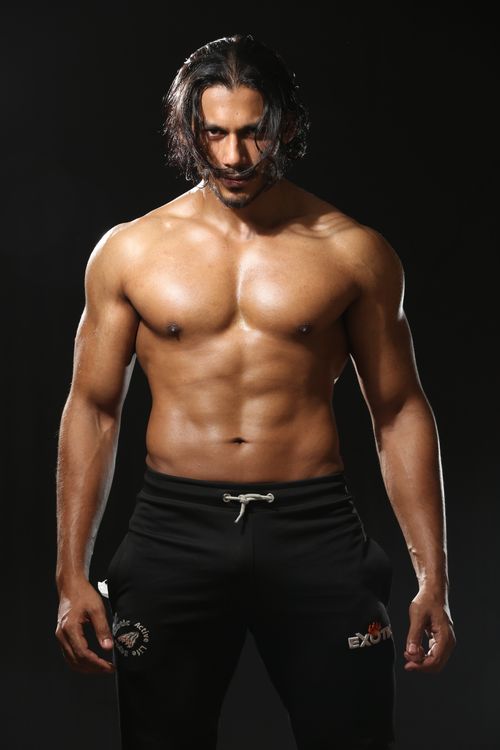 Free Intense portrait of a muscular man standing topless in athletic pants against a black backdrop. Stock Photo