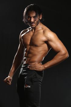 Portrait of a muscular topless man posing in a studio with a dark background.