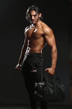 Portrait of a muscular man in sportswear holding a gym bag during a fashion photography studio shoot.