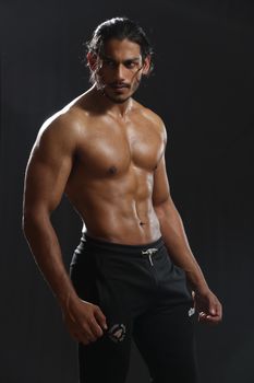 Powerful studio image of a muscular male model posing in sportswear against a dark background.